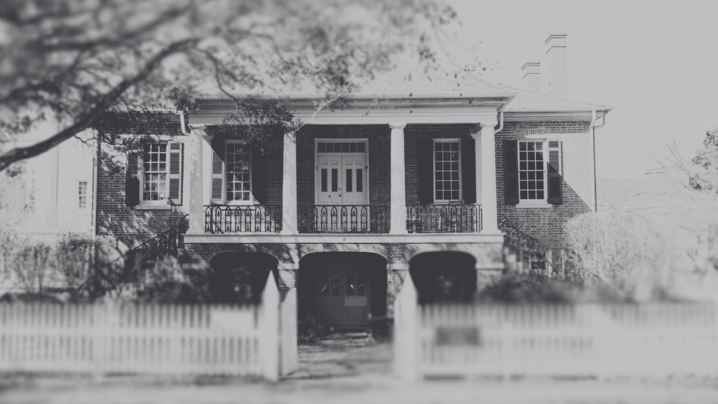 A black and white photograph of a historic two-story brick house with columns in Tuscaloosa, Alabama.