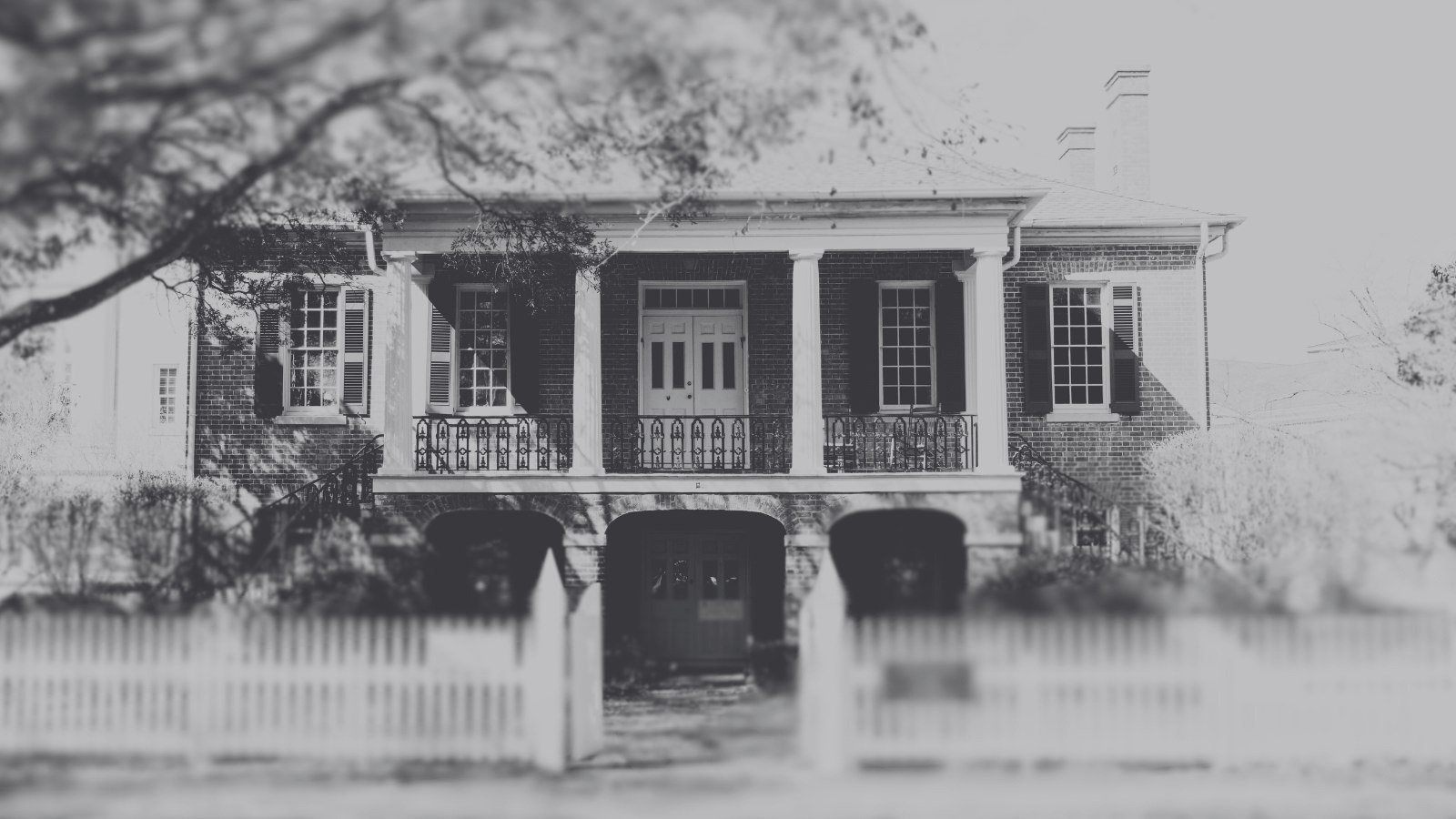 A black and white photograph of a historic two-story brick house with columns in Tuscaloosa, Alabama.